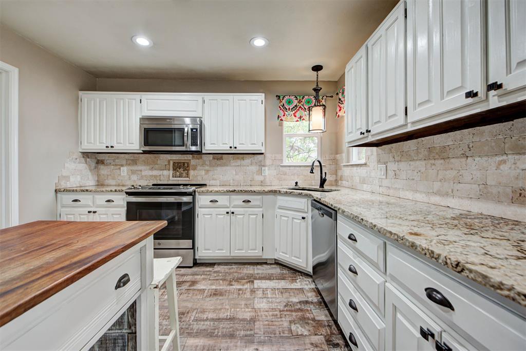 Kitchen with white cabinets, stone counters, stainless steel appliances, and a wood-topped island.