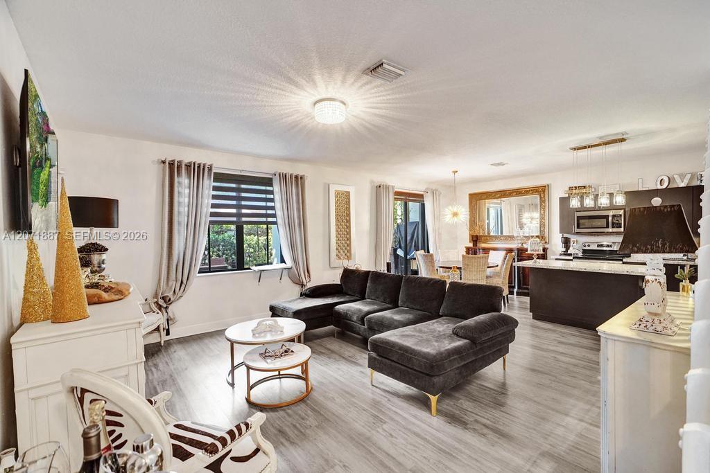 Open-plan living room with a charcoal sectional, large windows, and the kitchen and dining area beyond.