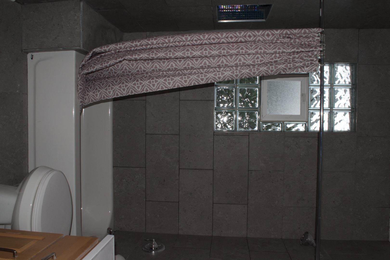 Bathroom with dark tiled walls, a glass-block window, and patterned fabric above the shower.