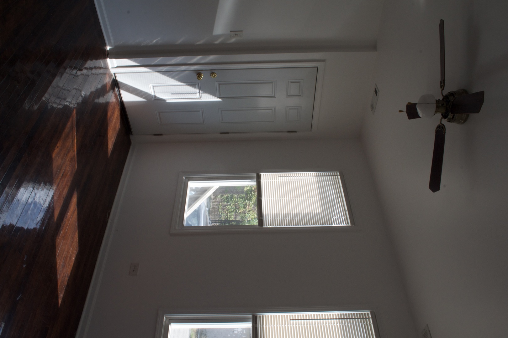 Vacant room with dark hardwood floors, a paneled door, window blinds, and a ceiling fan.