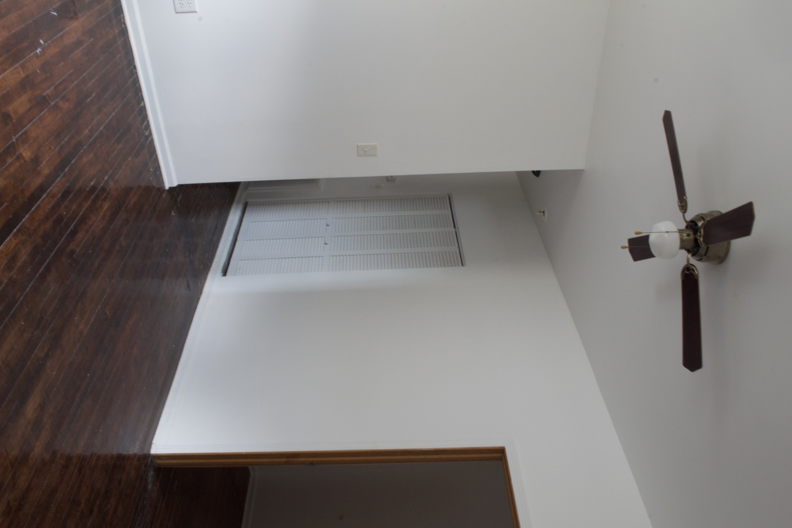 Empty room with dark wood flooring, a ceiling fan, and louvered closet doors.