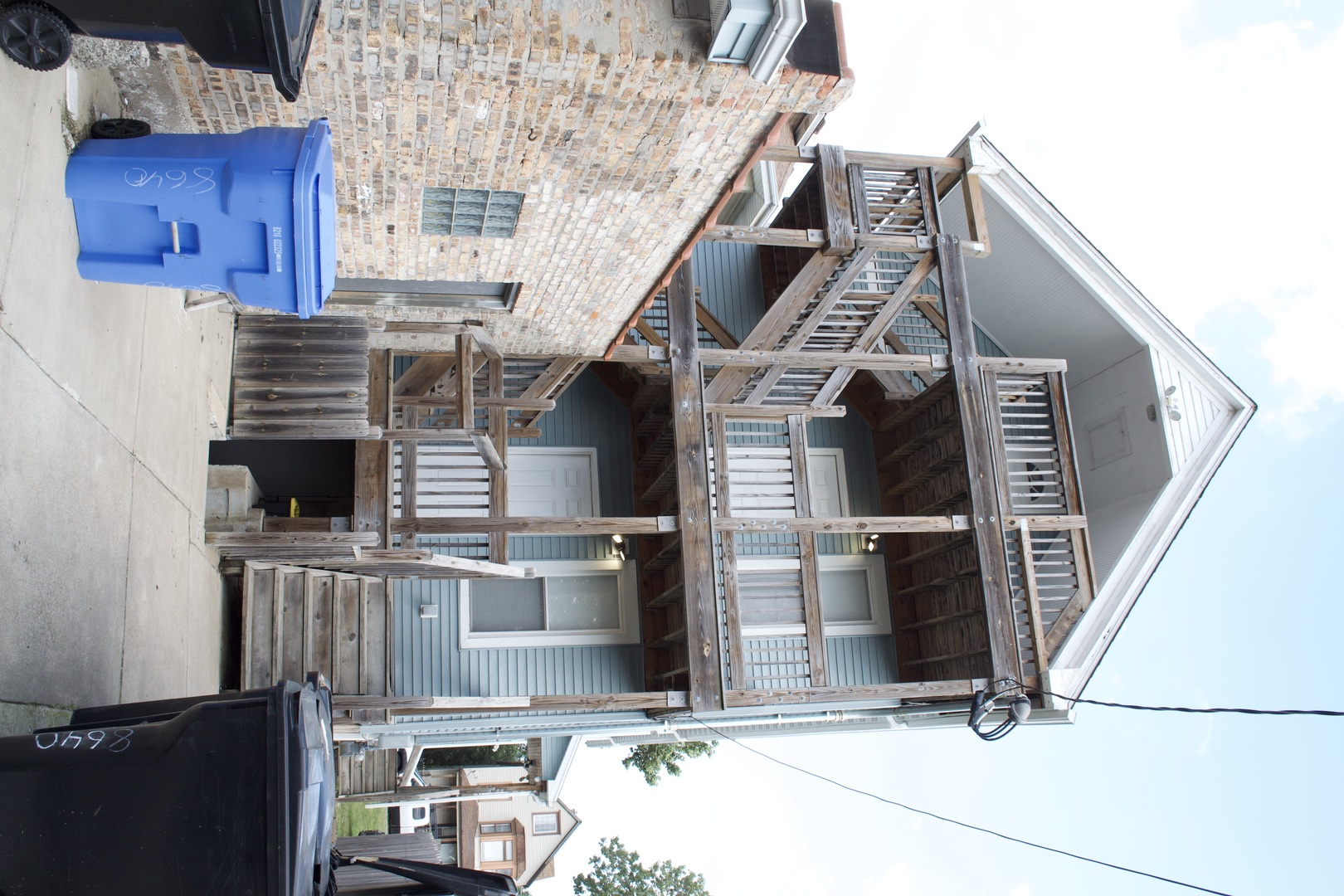 House exterior with extensive weathered wooden stairs and porches beside a brick wall.