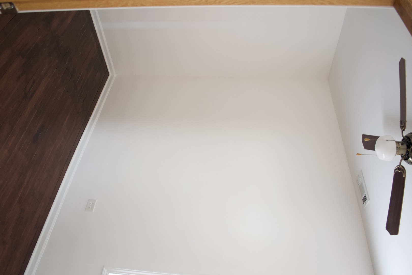 White room ceiling with a ceiling fan and dark wood flooring at the edge.
