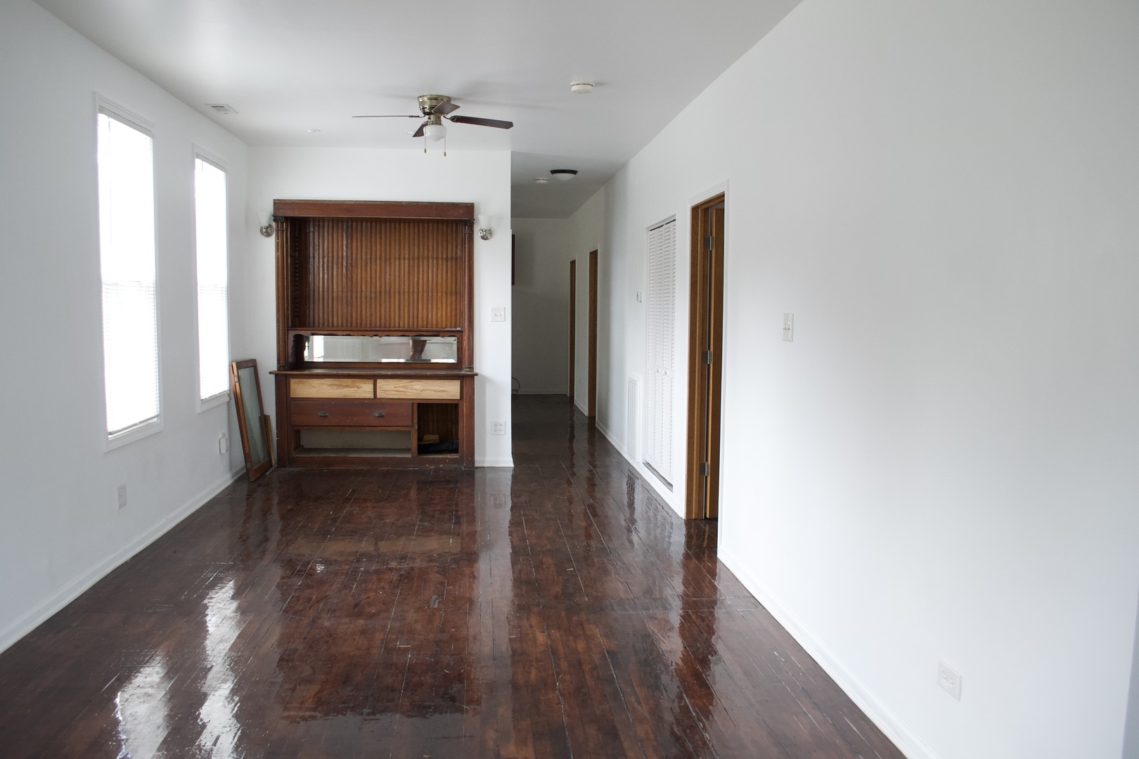 Empty living room with glossy dark hardwood floors and built-in wooden cabinetry.