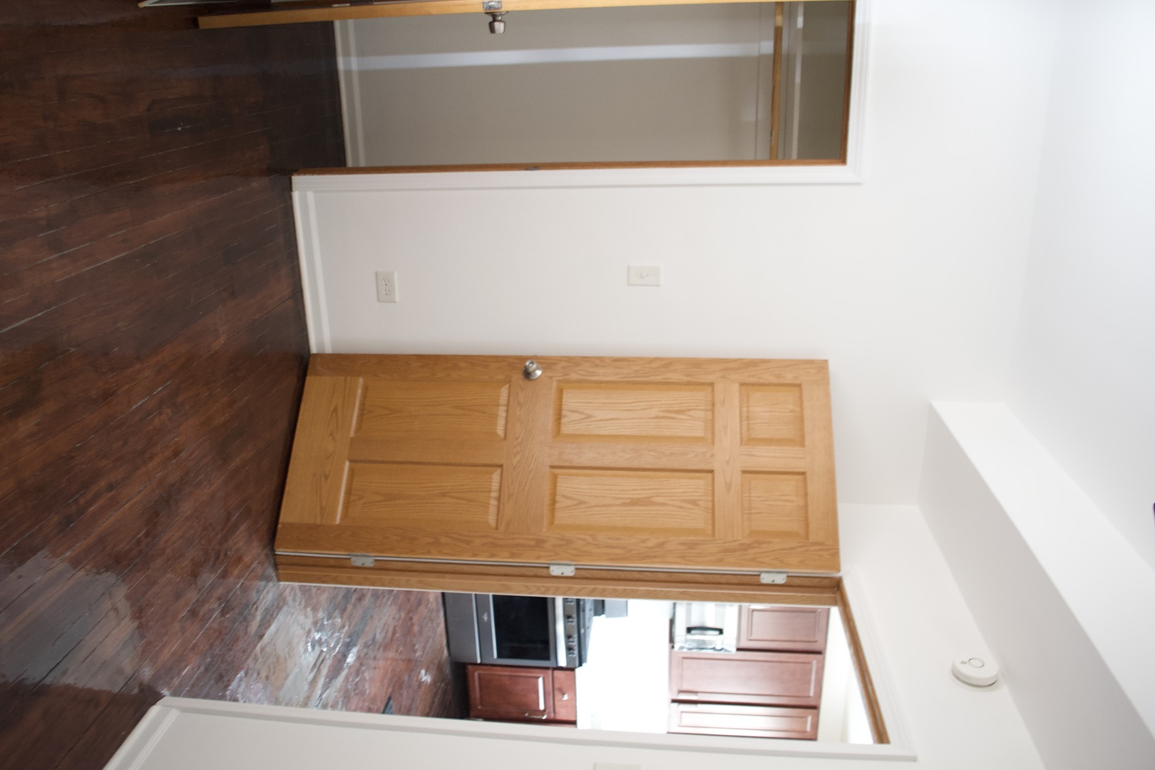 Wooden doorway opens toward a kitchen, with dark wood flooring and cabinetry.