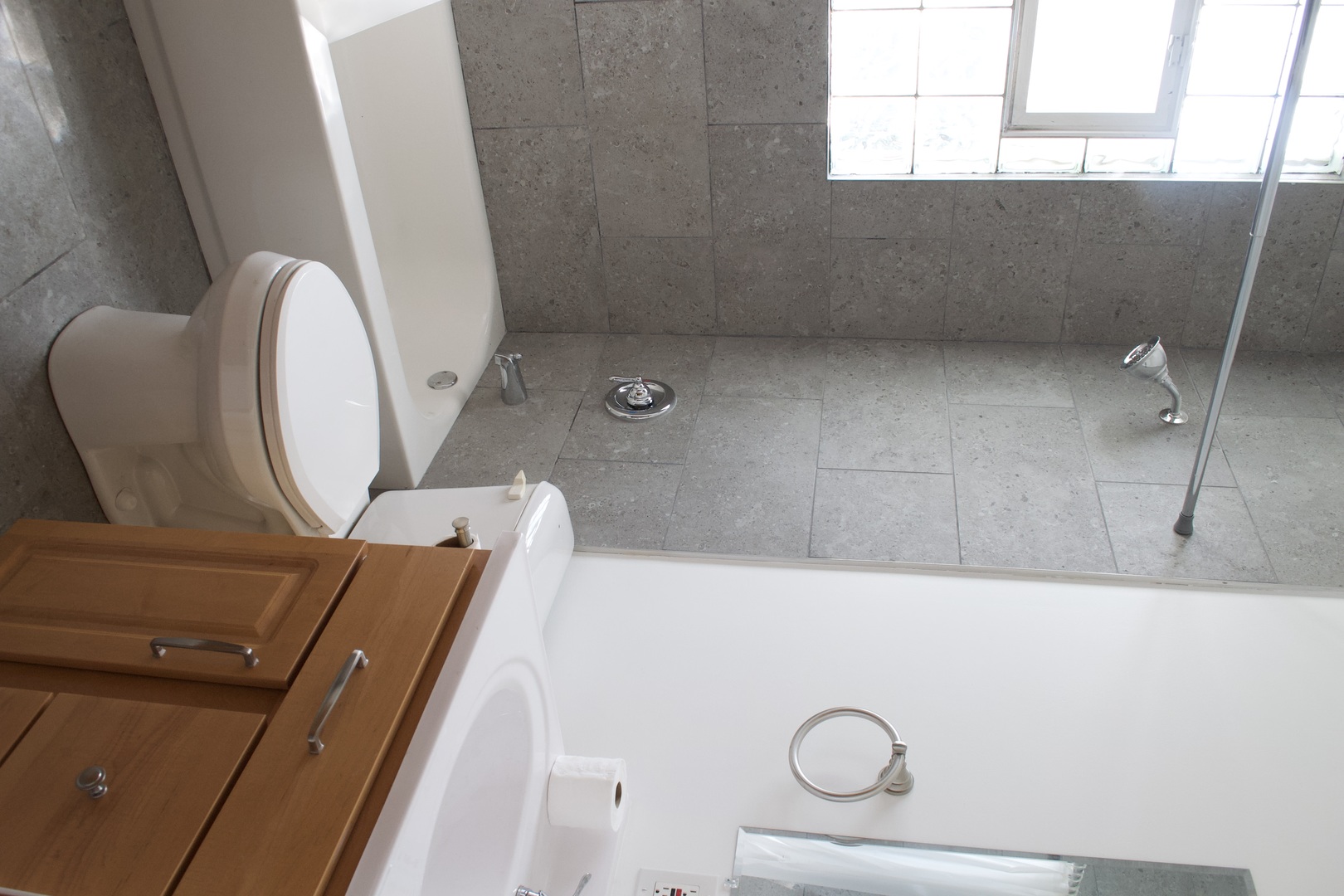 Bathroom with a white tub, glass-block window, gray tile, toilet, and wood vanity.