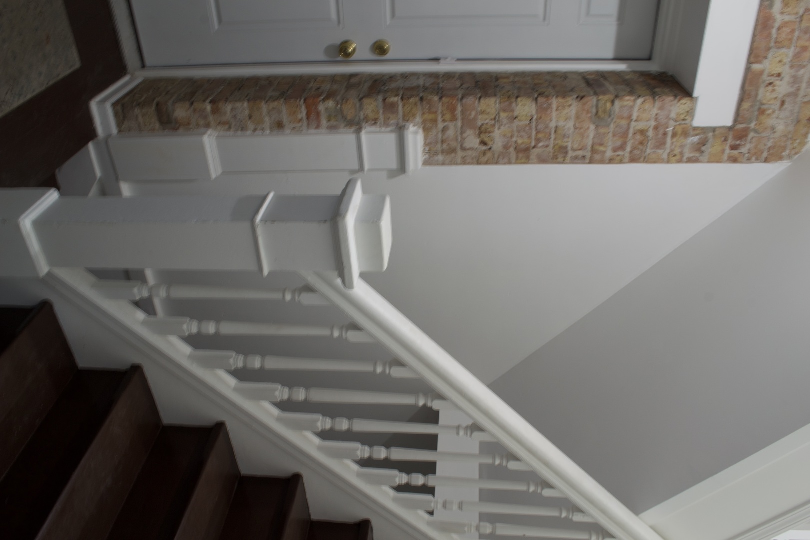 Dark wood staircase with white balusters beside a brick wall and paneled door.