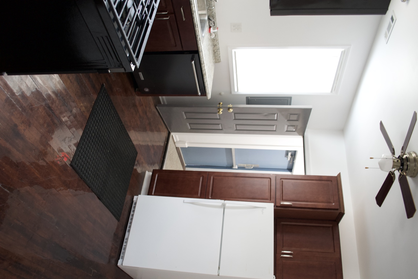 Kitchen with reddish-brown cabinets, white refrigerator, black stove, and dark wood flooring.