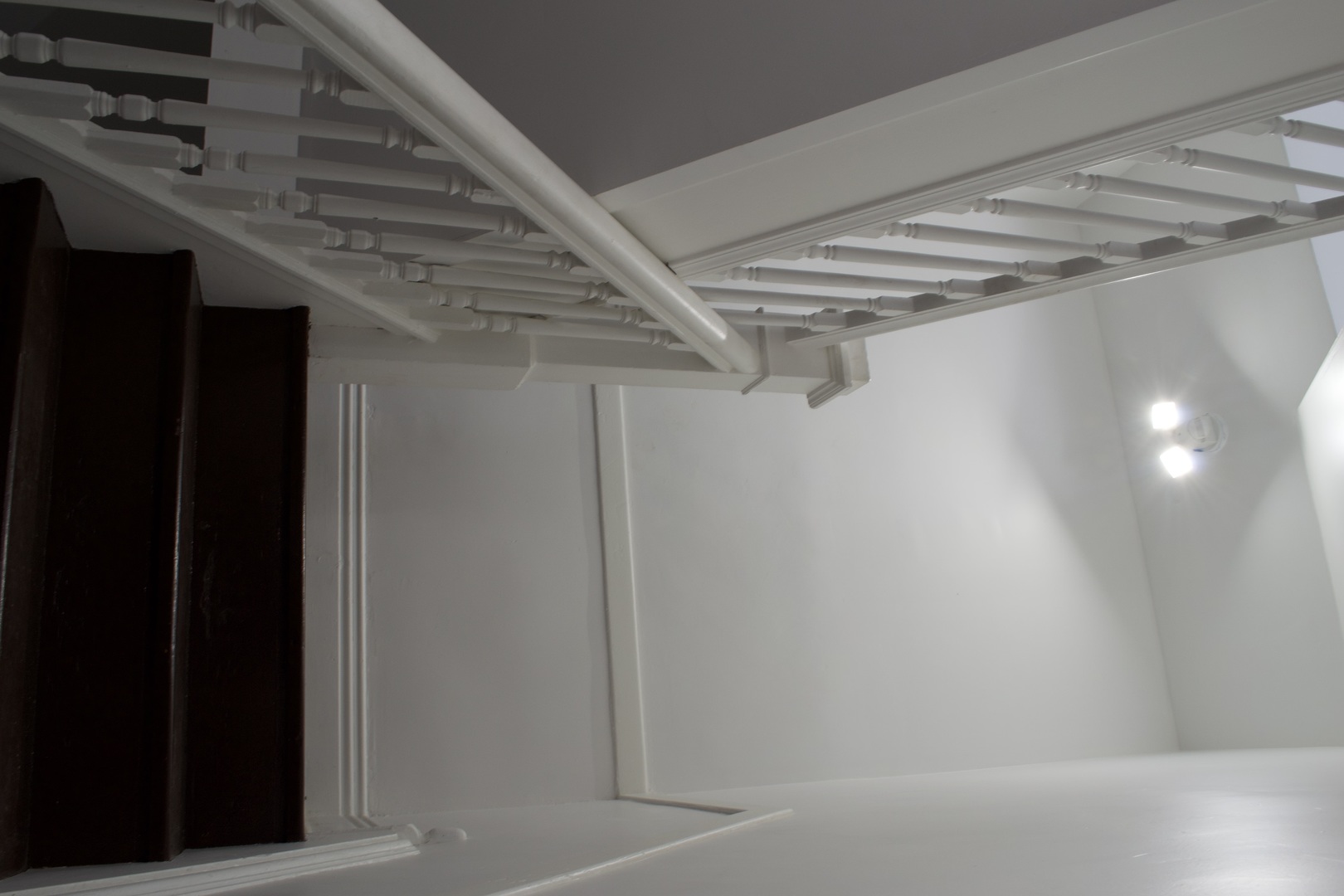 Staircase with dark wood steps, white railings, and wall lights.