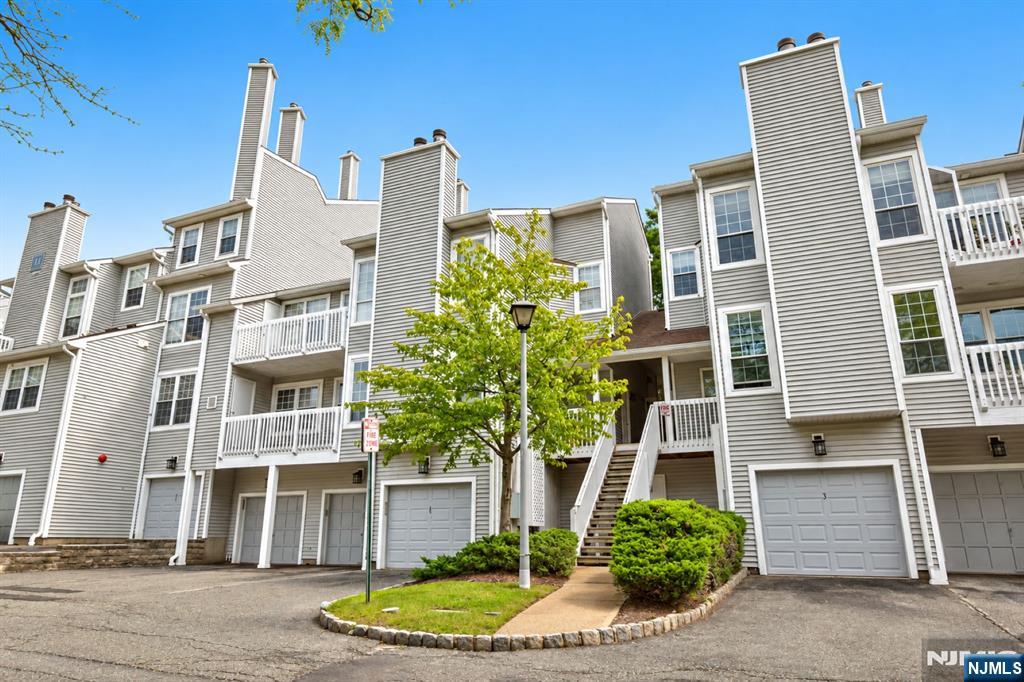 Gray multi-story townhouse building with white balconies, garage doors, and a landscaped entry island.