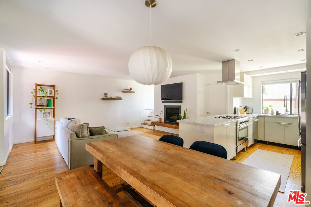 Open-plan kitchen and dining area with a white island, wooden table, hardwood floors, and fireplace.