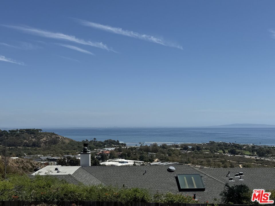 Ocean view from the property, with coastal hills, rooftops, and a broad blue sky.
