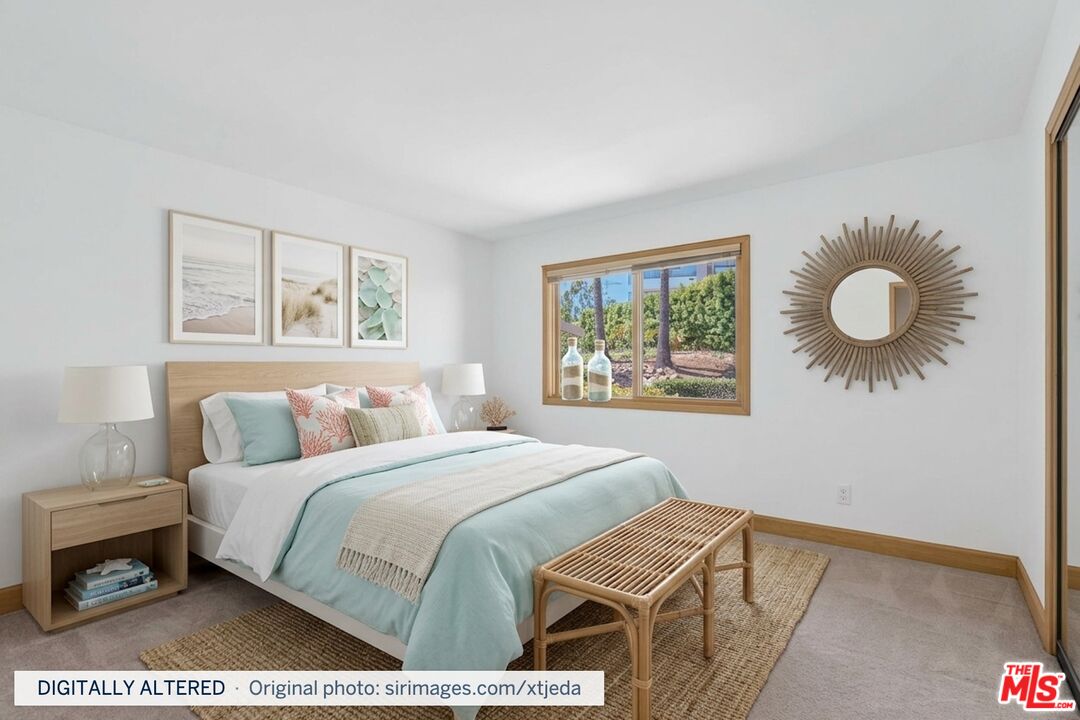 Staged bedroom with aqua bedding, a woven bench, coastal prints, and a window overlooking greenery.