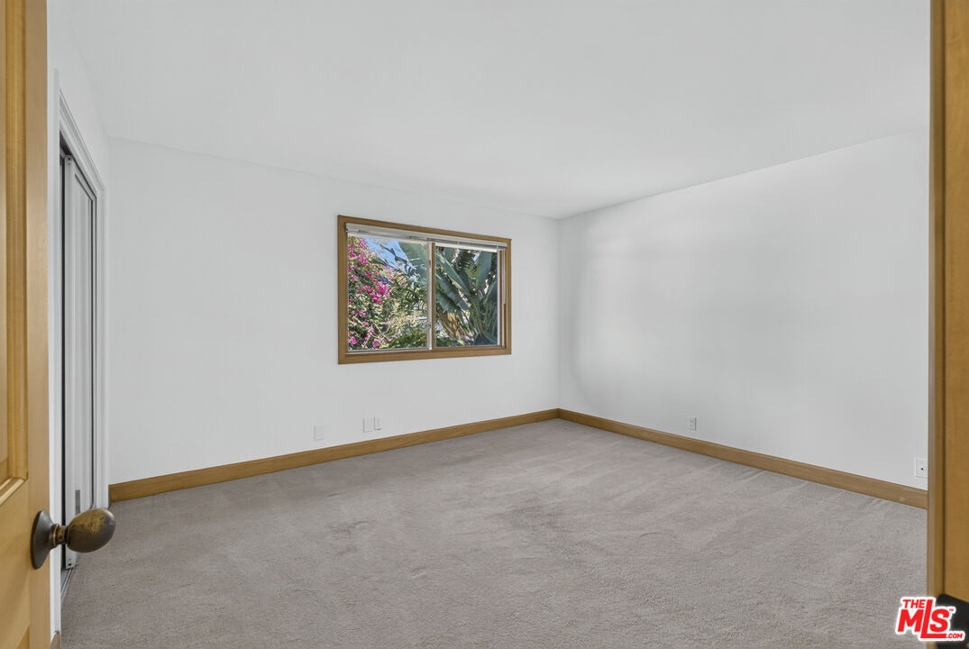 Empty carpeted room with wood trim and a window overlooking greenery.