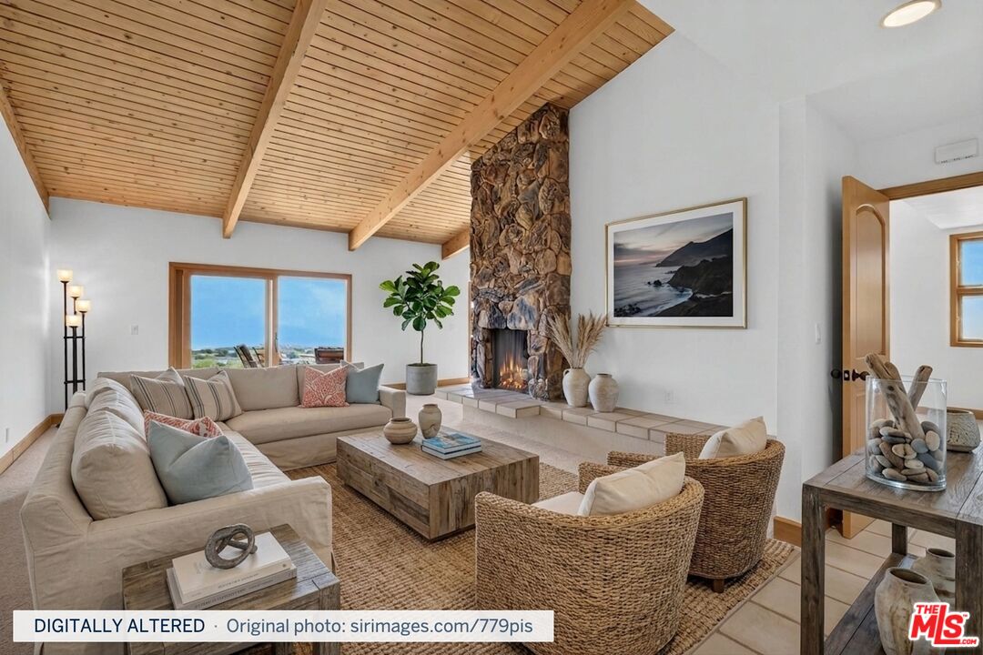 Living room with a vaulted wood ceiling, stone fireplace, and ocean views through the window.