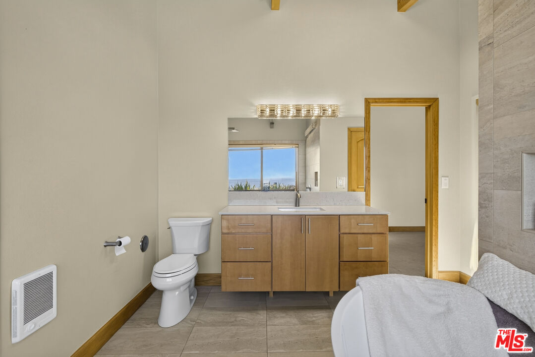 Bathroom with a wood vanity, wide mirror, and window showing a glimpse of the ocean.