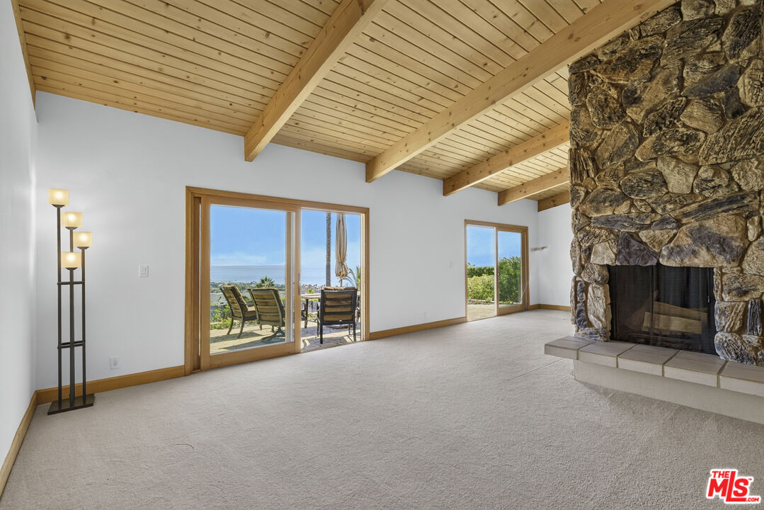 Living room with a vaulted wood ceiling, stone fireplace, and ocean views through sliding glass doors.