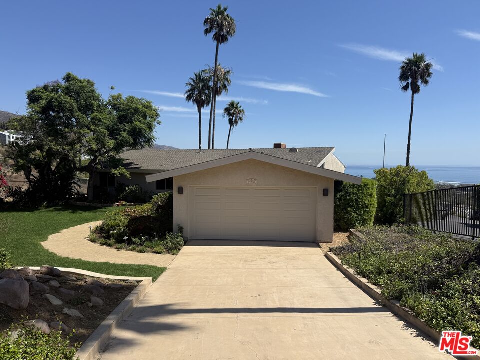 Single-story home with a wide driveway, two-car garage, tall palms, and an ocean glimpse.
