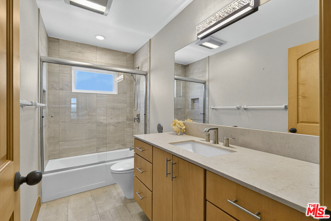 Bathroom with a glass-enclosed tub and shower, beige tile, and a wood vanity.