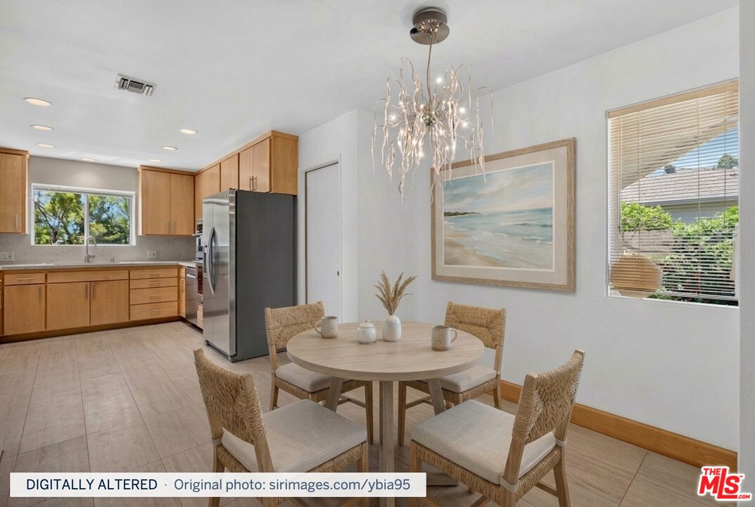 Kitchen and dining area with wood cabinetry, stainless refrigerator, round table, and sculptural chandelier.