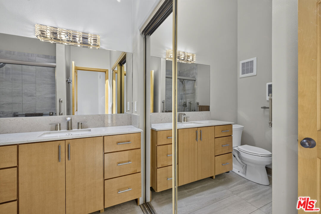 Bathroom with a light-wood double vanity, large mirrors, and a toilet beside the counter.