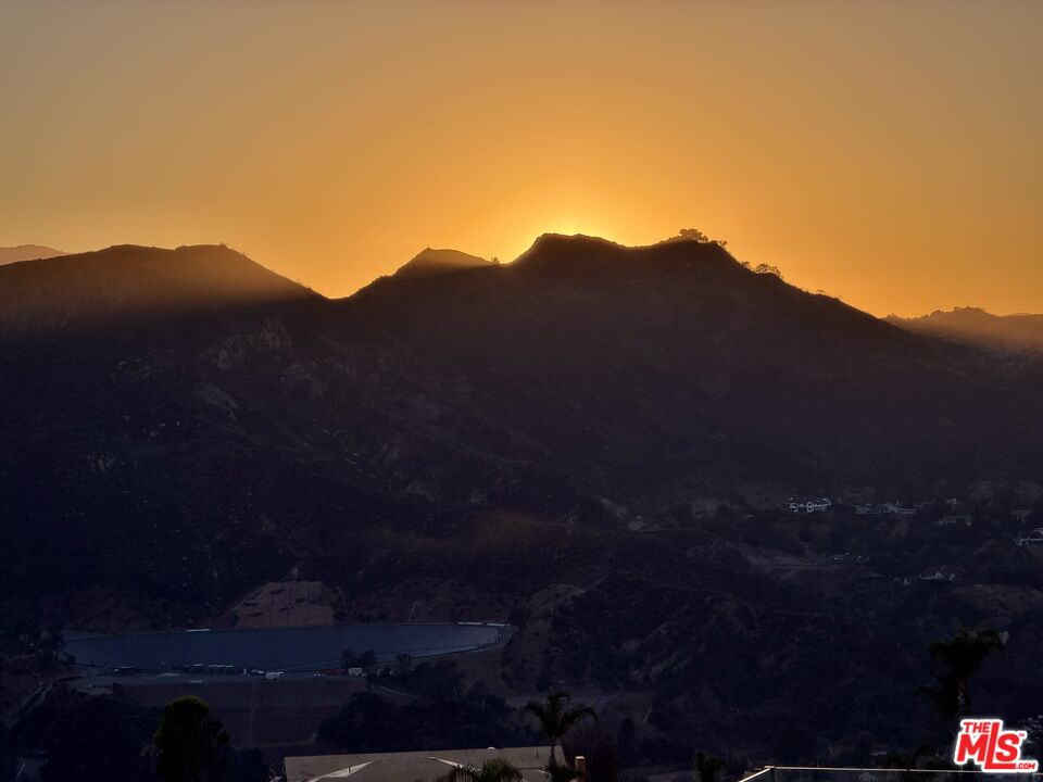 Mountain ridges silhouetted against a golden sunset, with a reservoir below.