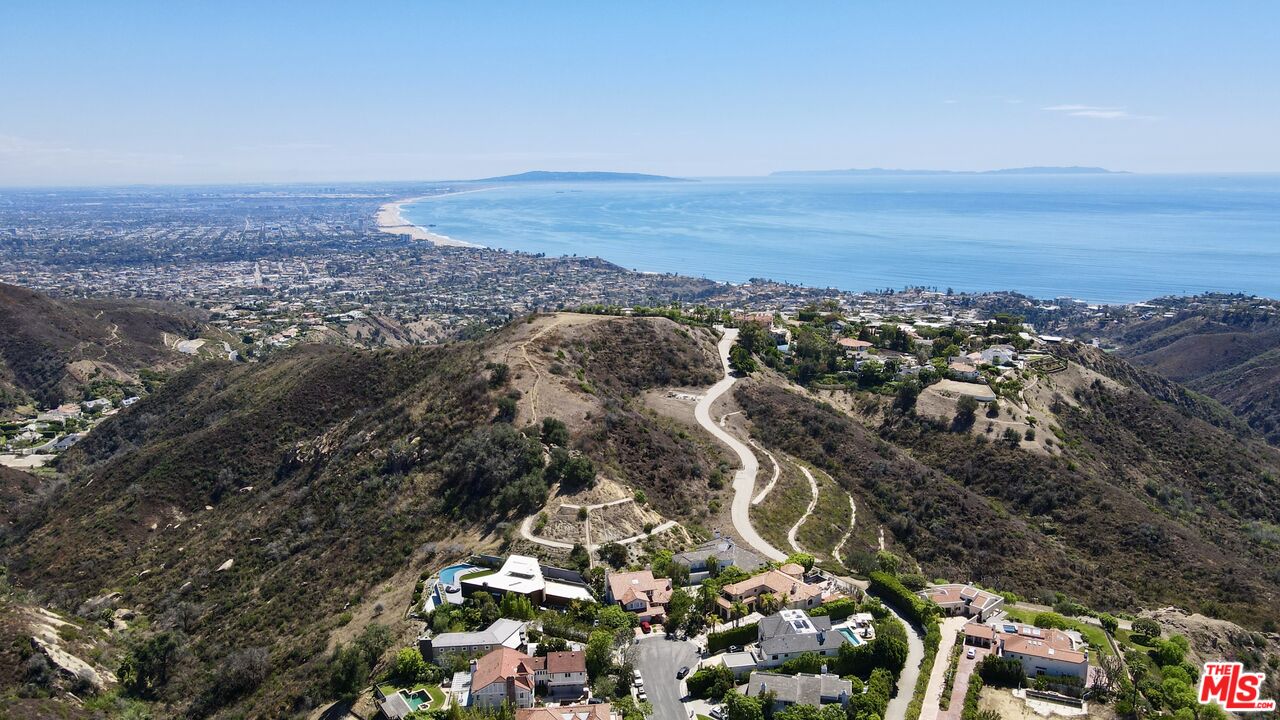 Hillside homes overlook the coastline, with a winding road and ocean in the distance.