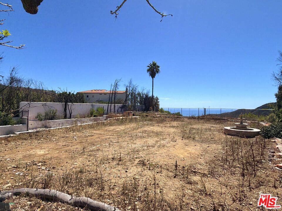 Undeveloped lot with a circular fountain and ocean view beyond the fence.