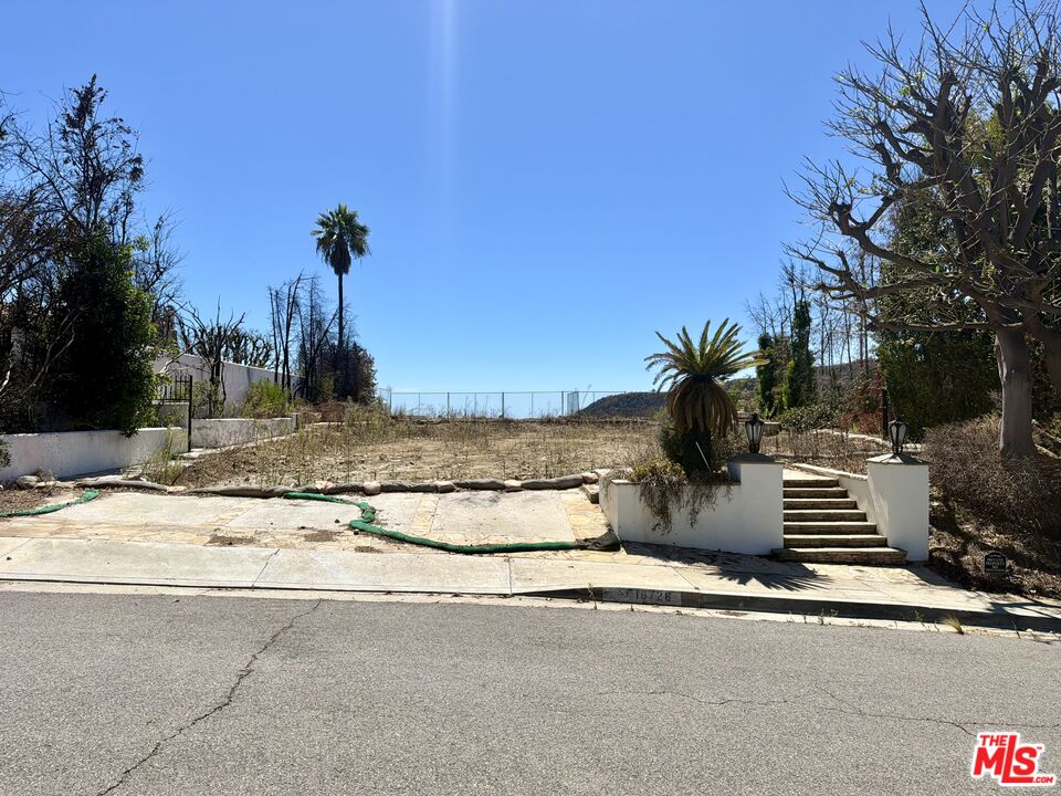 Vacant residential lot with stone entry steps, palm trees, and a distant hillside.