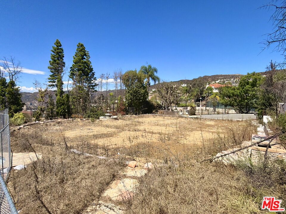 Vacant lot with dry ground, mature trees, and distant hillside views.