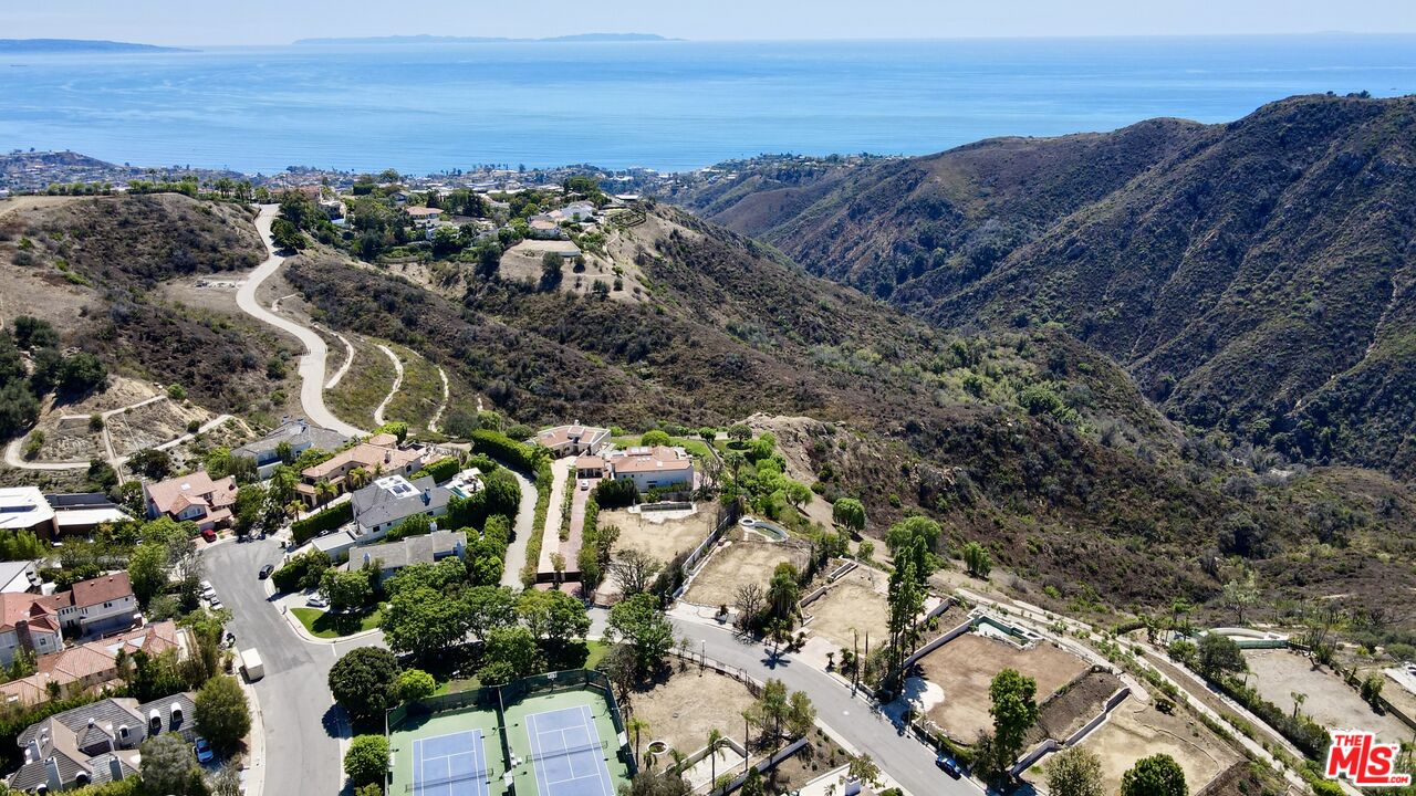 Aerial view of hillside homes and winding roads overlooking rugged hills and the ocean.