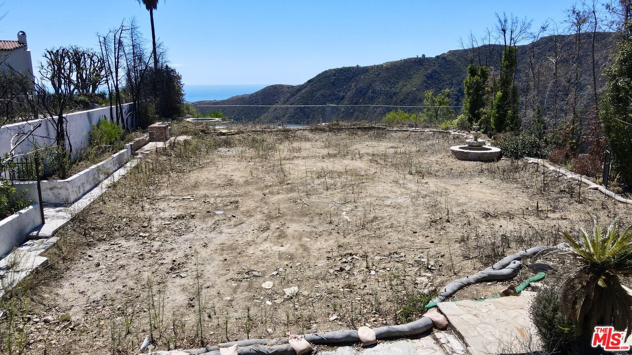 Mostly bare backyard with stone borders, a circular feature, hillside, and ocean glimpse.