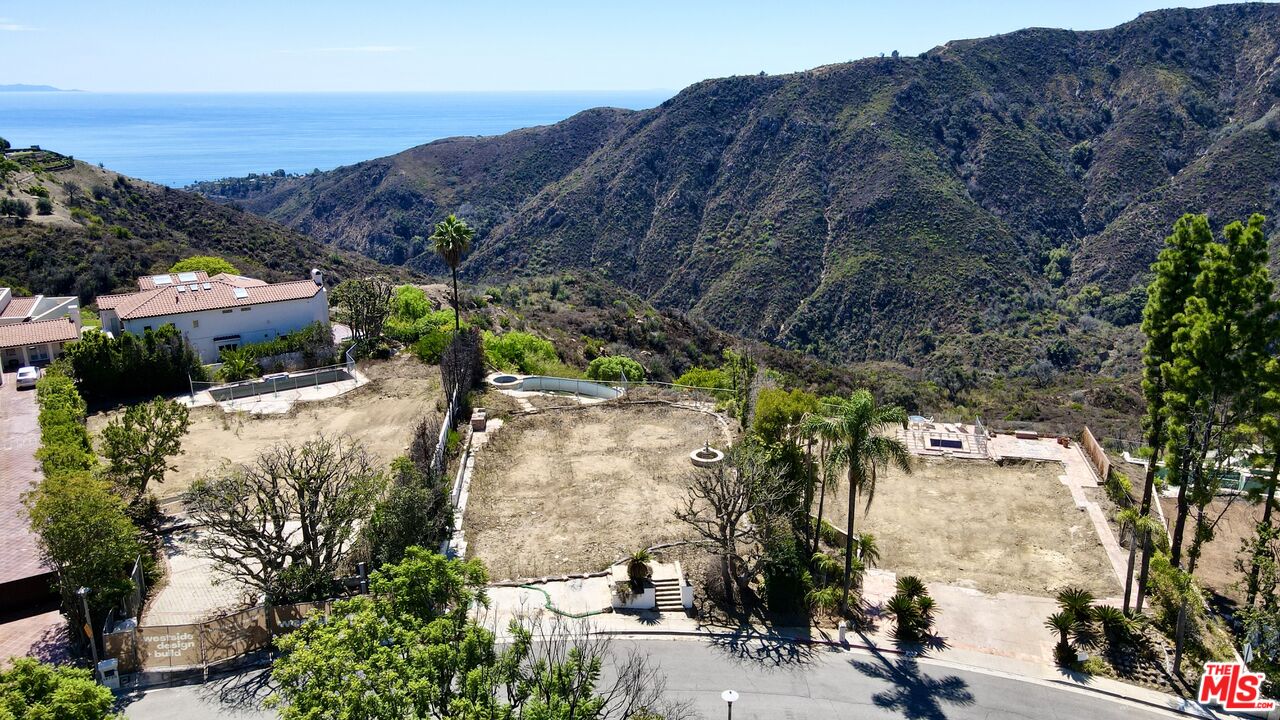 Cleared hillside lot with a small pool, overlooking rugged mountains and the Pacific Ocean.