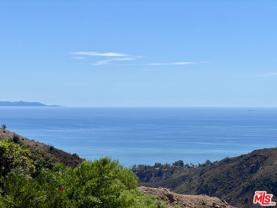 Ocean view from coastal hills, with green hillside foreground and distant coastline.