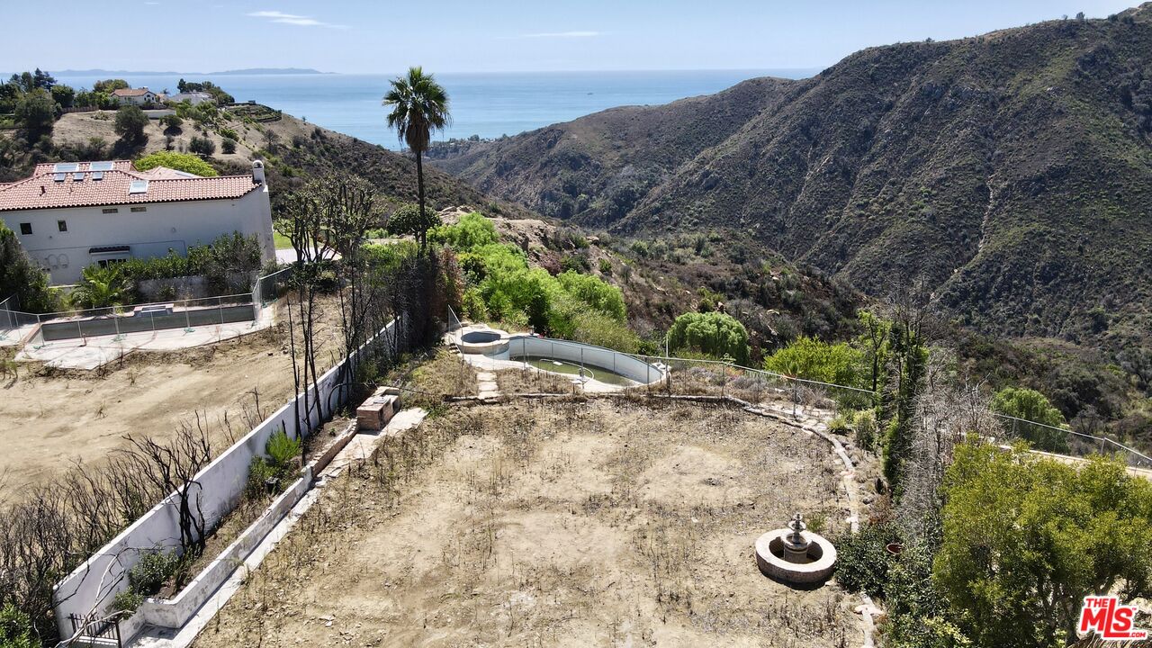 Cleared hillside lot with a pool, neighboring home, mountains, and ocean views.