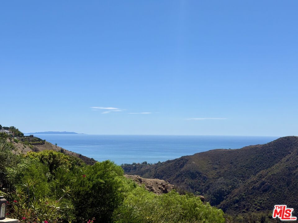 Ocean view framed by green hillside shrubs and rugged coastal hills.