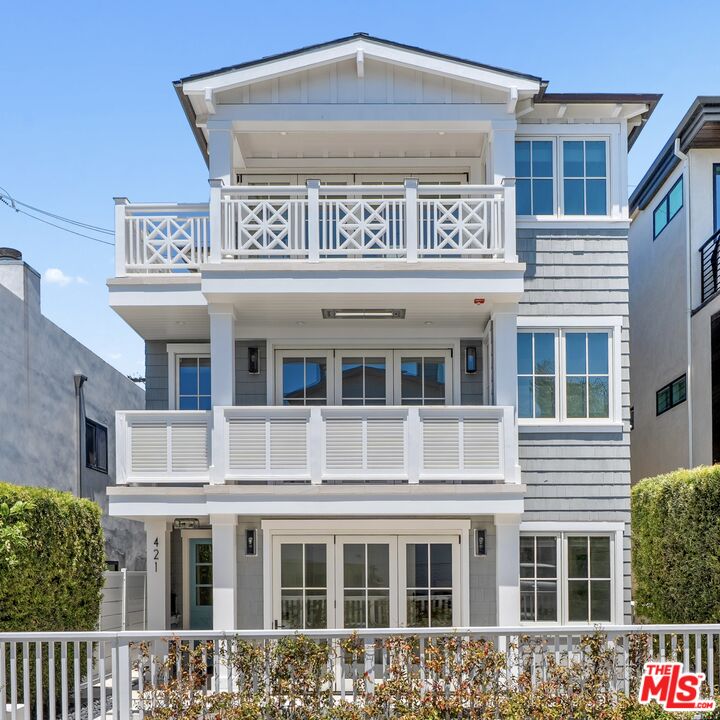 Three-story gray-shingled home with white balconies, large windows, and a gated front garden.