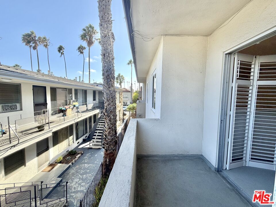 Apartment balcony overlooking a shared courtyard with neighboring units and tall palm trees.