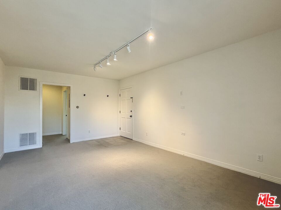 Unfurnished carpeted room with track lighting and a tiled entry area.