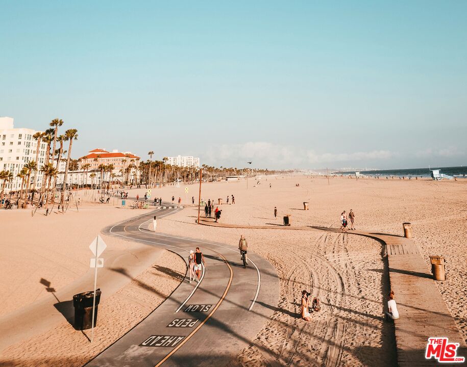 Sandy beach with a curving bike path, palm trees, beachfront buildings, and ocean.