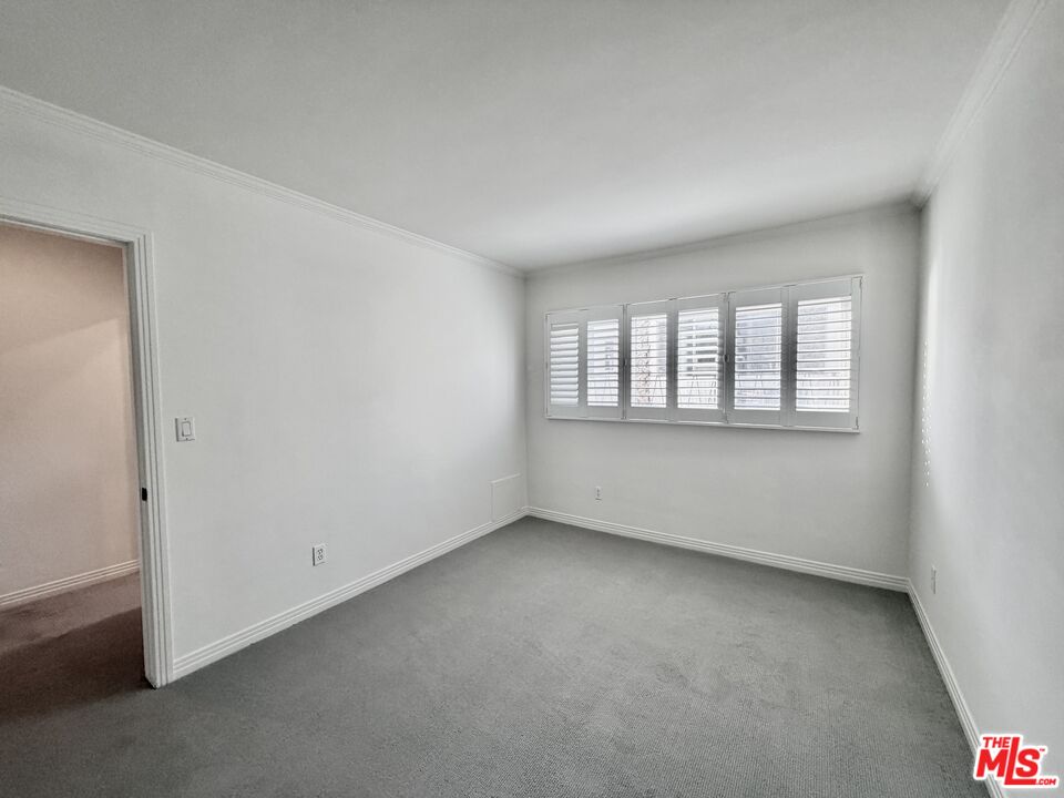 Empty bedroom with gray carpet and a wide window fitted with white plantation shutters.