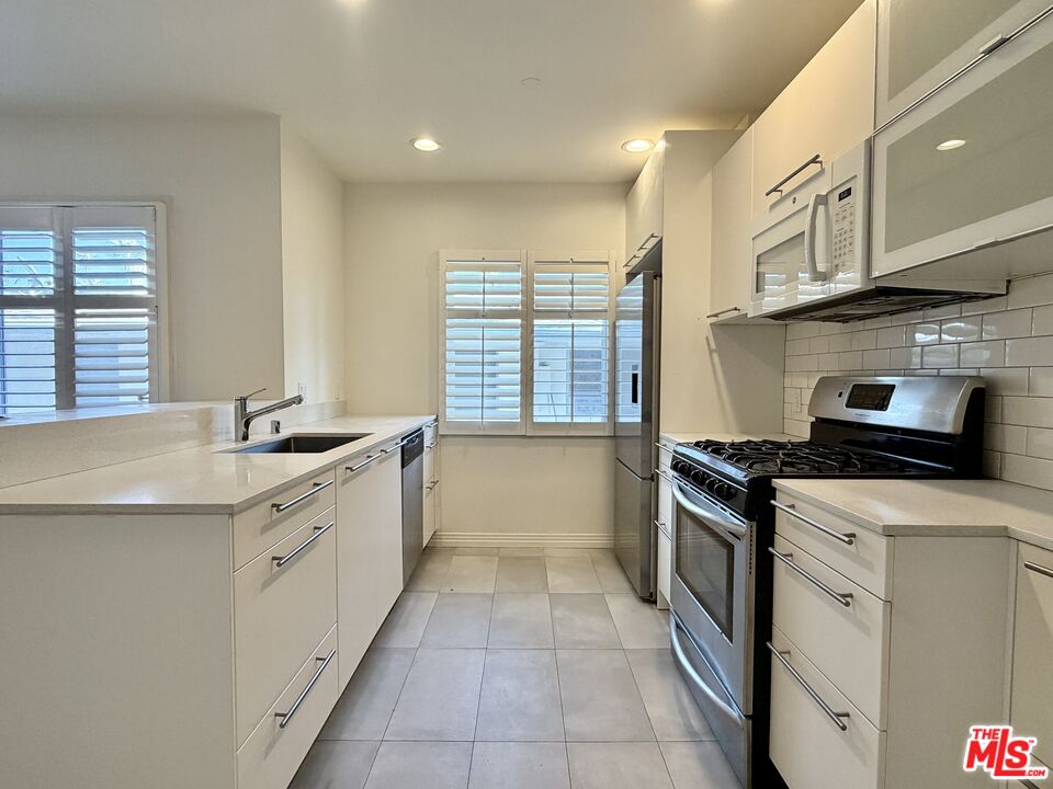 Galley kitchen with white cabinetry, stainless-steel appliances, and shuttered windows.