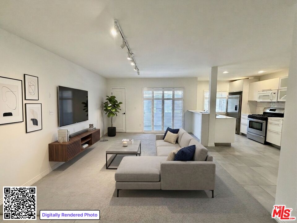 Staged living room with a gray sectional, wall-mounted television, and open kitchen.