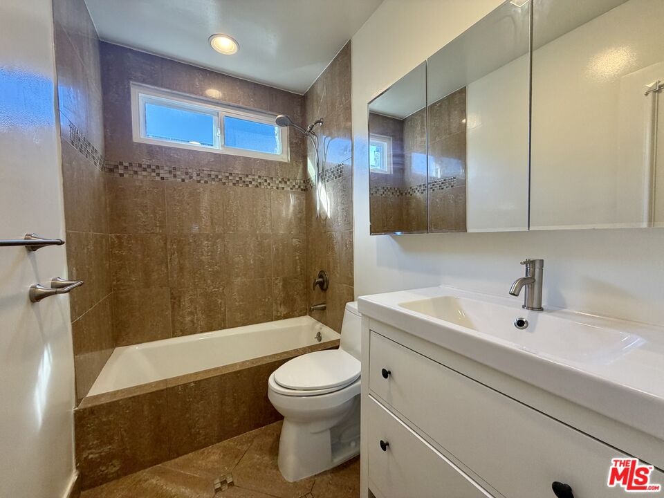 Bathroom with a tiled tub and shower, high window, and white vanity with mirrored cabinet.