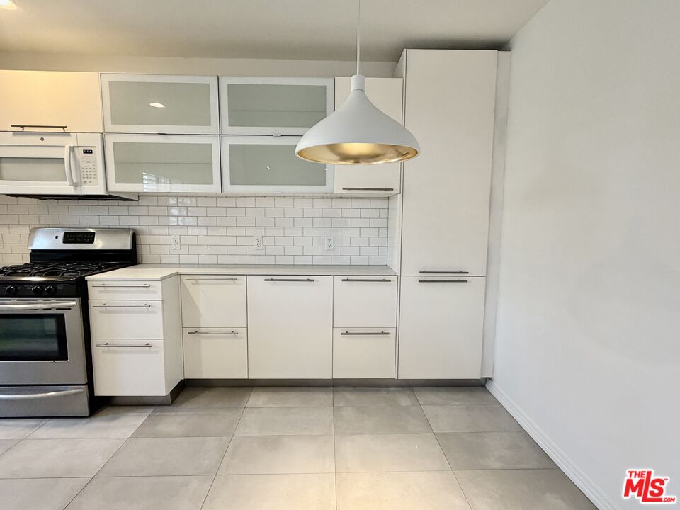 Modern white kitchen with subway tile backsplash, stainless steel range, and large pendant light.