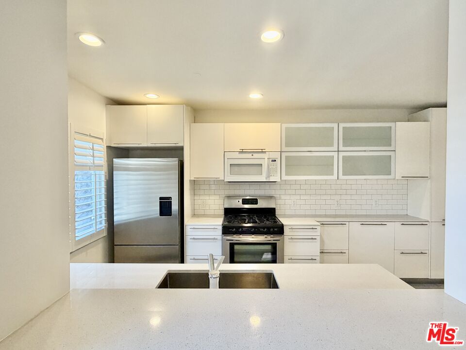 Modern white kitchen with stainless steel appliances and a wide island with double sink.