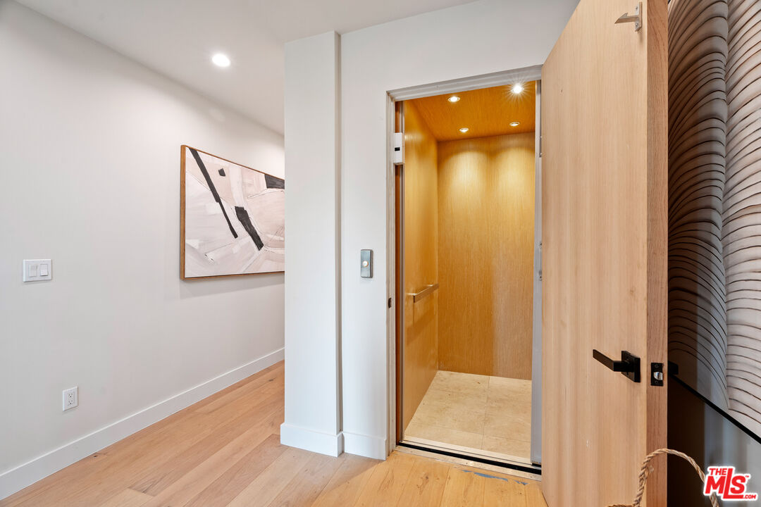 Open wood-paneled elevator beside a light wood door and abstract wall art.