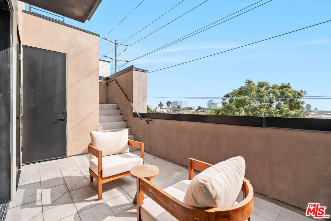 Rooftop terrace with cushioned wooden chairs, tiled floor, and distant city buildings.