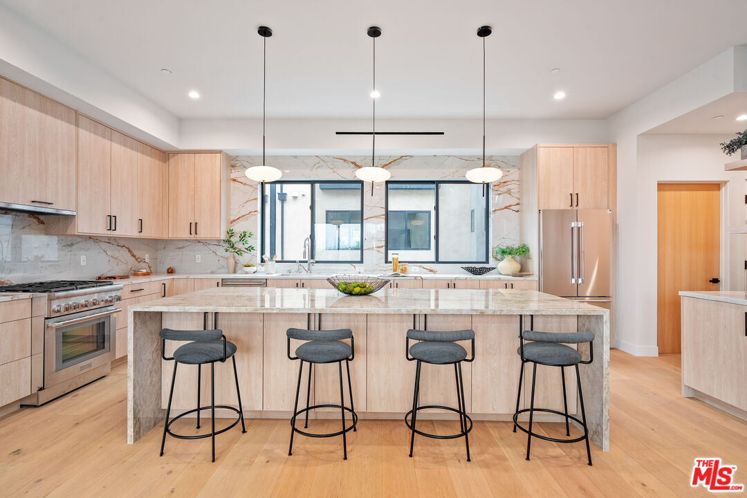 Modern kitchen with a marble island, four stools, light wood cabinetry, and pendant lights.
