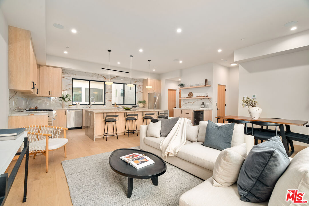 Open-plan living room and kitchen with light wood cabinetry, marble-look surfaces, and a white sectional sofa.